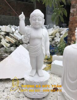 Tượng Phật Đản Sanh đá cẩm thạch trắng tự nhiên trước đống đổ nát.