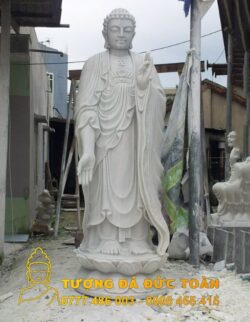 Tượng Phật A Di Đà đá nguyên khối màu trắng làm từ đá nguyên khối ở phía trước một tòa nhà.