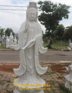 Tượng Tượng Quan Âm đứng đài sen đá đẹp màu trắng trước một con phố.