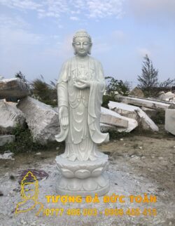 Bán tượng Phật A Di Đà đá cẩm thạch trắng trước một đống gạch vụn.