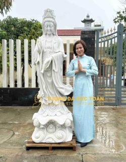 Một người phụ nữ đang đứng cạnh bức tượng phật trắng.