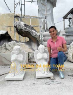 Một người phụ nữ đang tạo dáng bên cạnh hai bức tượng thiên thần.