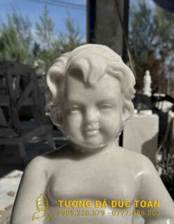 Bức tượng em bé màu trắng đang ngồi trên bàn.