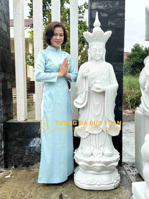 Một người phụ nữ đang đứng cạnh bức tượng phật.
