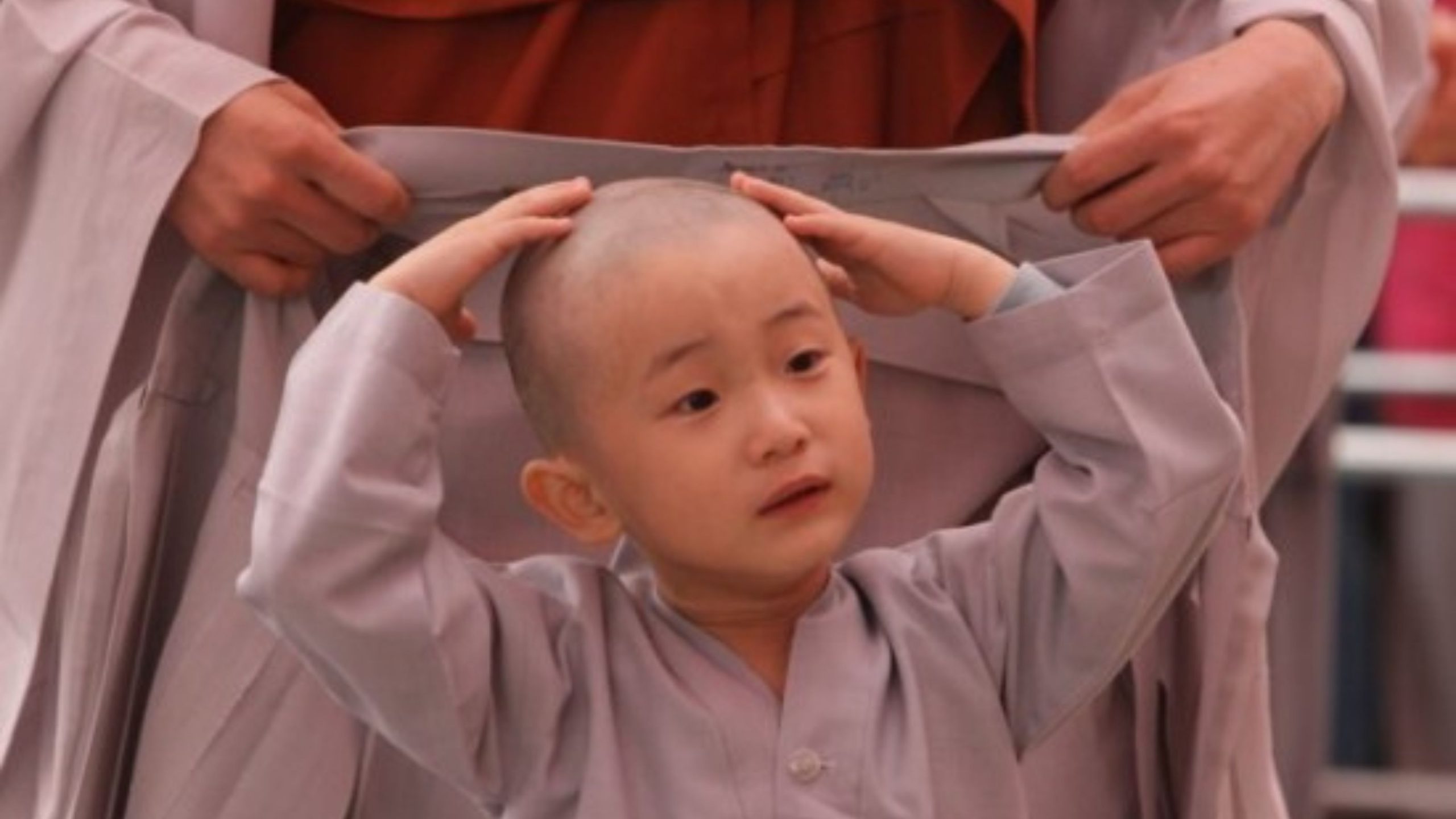 Một em bé chú tiểu mặc áo choàng với cái đầu cày.